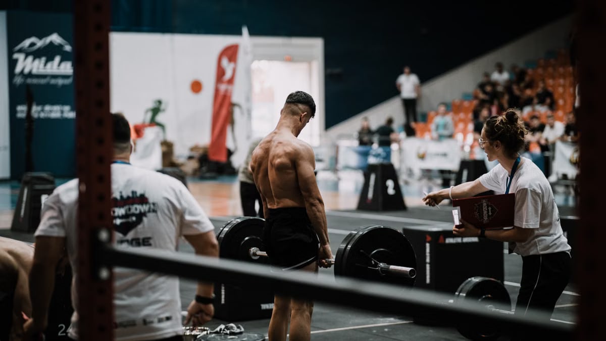 A weightlifting athlete prepares for a lift during a competition with judges observing.